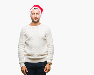 Young handsome man wearing santa claus hat over isolated background with serious expression on face. Simple and natural looking at the camera.