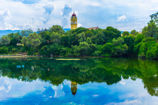 Picturesque view of Karavomilos lake at Sami in Kefalonia ionian island of Greece. Perfect reflection of the claoudscape, the trees and church on the calm waters of the lake