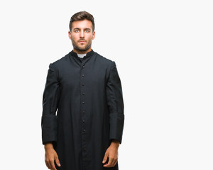 Young catholic christian priest man over isolated background with serious expression on face....