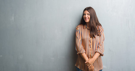 Young brunette woman over grunge grey wall looking away to side with smile on face, natural expression. Laughing confident.