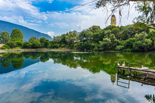 Picturesque view of Karavomilos lake at Sami in Kefalonia ionian island of Greece. Perfect reflection of the claoudscape, the trees and church on the calm waters of the lake. 