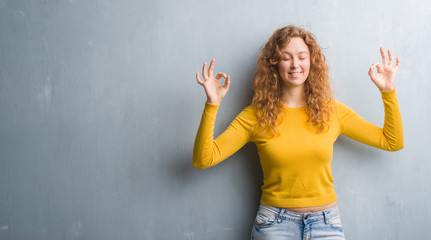 Young redhead woman over grey grunge wall relax and smiling with eyes closed doing meditation gesture with fingers. Yoga concept.