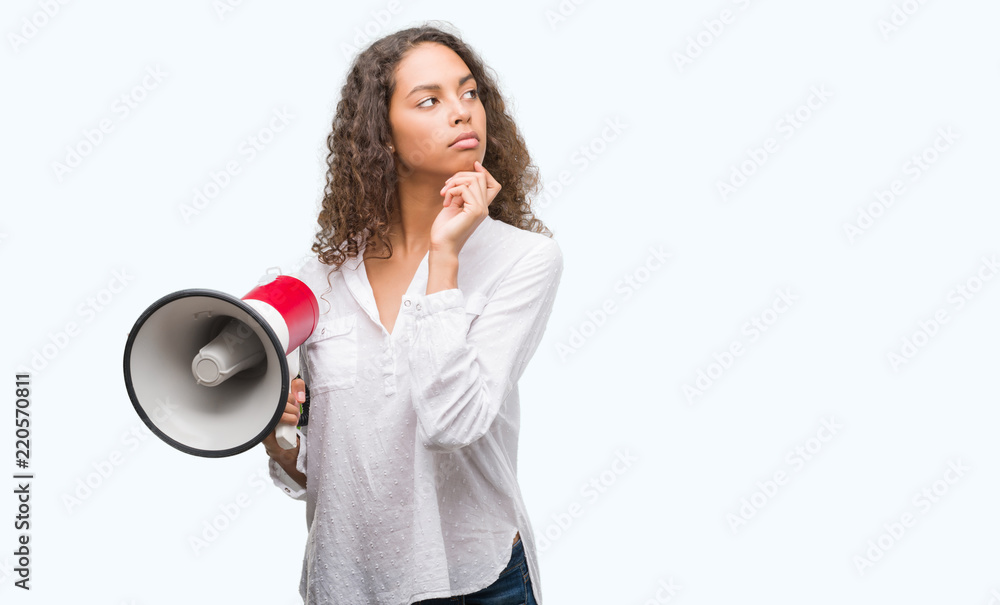 Wall mural young hispanic woman holding megaphone serious face thinking about question, very confused idea