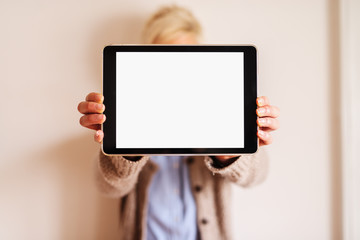 Close up of focus view of tablet with white editable screen . Blurred picture of a woman standing behind tablet and holding it.