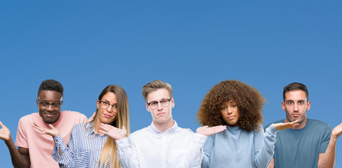 Composition of group of friends over blue blackground clueless and confused expression with arms...