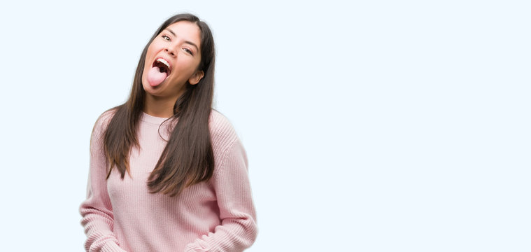Young beautiful hispanic woman wearing a sweater sticking tongue out happy with funny expression. Emotion concept.