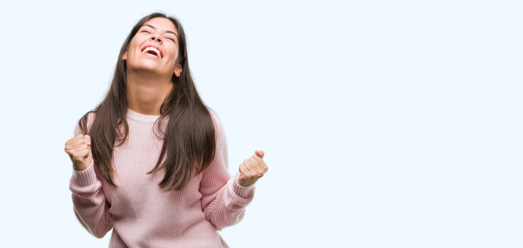 Young beautiful hispanic woman wearing a sweater very happy and excited doing winner gesture with arms raised, smiling and screaming for success. Celebration concept.