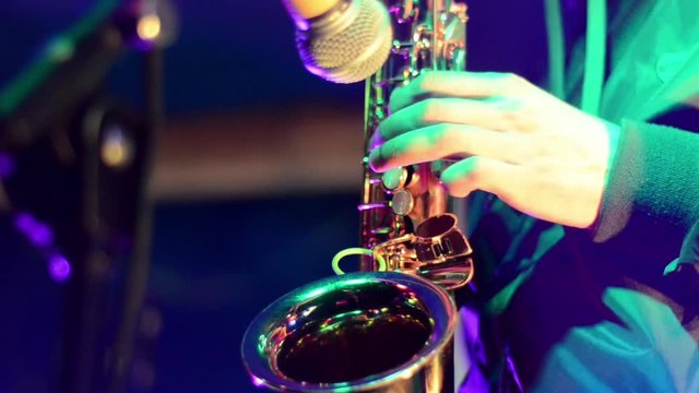 Musician playing saxophone on rock concert. A Man plays saxophone on festival. Tenor and alto saxophonists. Rehearsal on stage with light. Young Man playing Saxophone