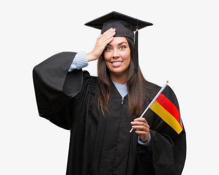 Young hispanic woman wearing graduated uniform holding flag of germany stressed with hand on head, shocked with shame and surprise face, angry and frustrated. Fear and upset for mistake.