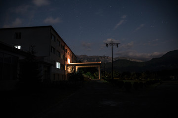 Mountain night landscape of building at forest at night with moon or vintage country house at night with clouds and stars. Summer night.