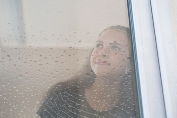 Young woman staring out of a wet window