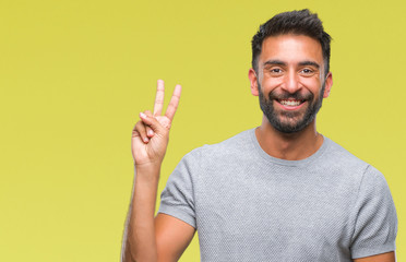 Fototapeta premium Adult hispanic man over isolated background smiling with happy face winking at the camera doing victory sign. Number two.