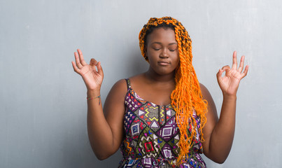 Young african american woman over grey grunge wall wearing orange braids relax and smiling with eyes closed doing meditation gesture with fingers. Yoga concept.
