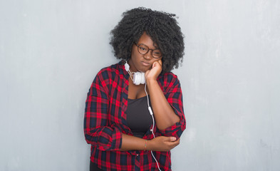 Young african american woman over grey grunge wall wearing headphones thinking looking tired and bored with depression problems with crossed arms.