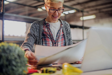 Cute young blond female designer looking at paper projects in her workshop.