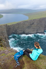 AERIAL: Hiker girl sits on the edge of a cliff and looks at the lake and ocean.