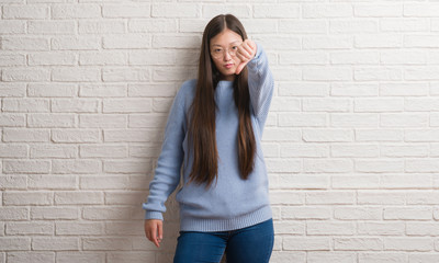 Young Chinise woman over white brick wall looking unhappy and angry showing rejection and negative with thumbs down gesture. Bad expression.