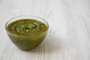 Bowl of freshly made basil pesto on white wooden table, side view. Close-up. Copy space.