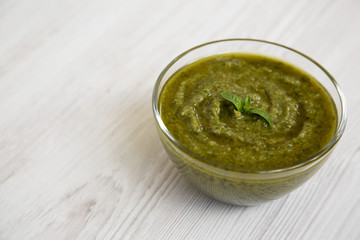 Bowl of freshly made basil pesto on white wooden surface, side view. Closeup. Copy space.