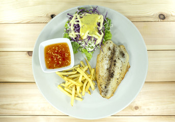 Grilled Fish Steak with Seafood Sauce in a white dish on a wooden background props decoration with French fries, green salad, purple cauliflower,Top view