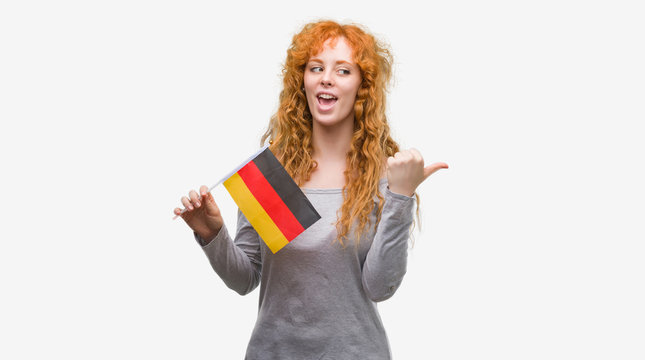 Young redhead woman holding flag of Germany pointing and showing with thumb up to the side with happy face smiling