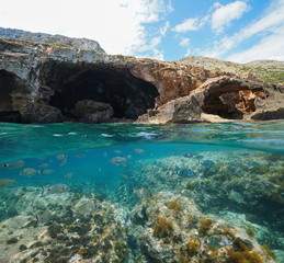 Fototapeta na wymiar Rocky coast with large cave on the sea shore and fishes underwater, split view above and below water surface, Mediterranean, Cova Tallada, Costa Blanca, Javea, Alicante, Valencia, Spain