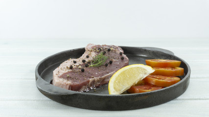 Fresh raw Striploin beef steaks in frying pan on white wood floor background props decoration tomato, lemon, black pepper, Front view with copy space for your text.