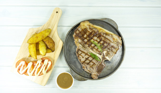 Grilled T-bone Steak In Frying Pan On White Wood Floor Background.Top View With Copy Space For Your Text.