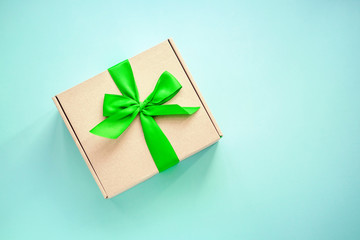 One craft paper box  with green ribbon bow on blue background from above. Minimalism, copy space