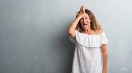 Middle age hispanic woman standing over grey grunge wall surprised with hand on head for mistake, remember error. Forgot, bad memory concept.