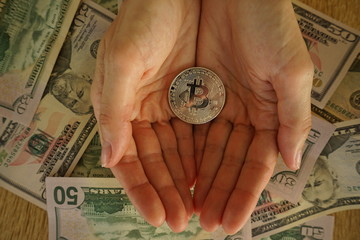 The golden bitcoin in hands on top of dollar banknote background.