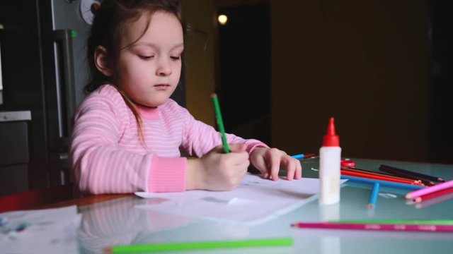 Adorable little Caucasian girl in pink sweater drawing shapes with a pencil on a sheet of paper, talking to someone.