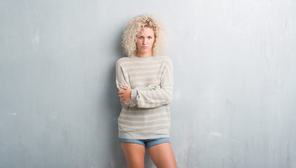 Young blonde woman with curly hair over grunge grey background skeptic and nervous, disapproving expression on face with crossed arms. Negative person.