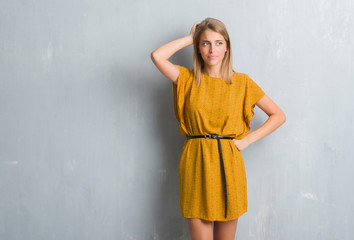 Fototapeta premium Beautiful young woman standing over grunge grey wall wearing a dress confuse and wonder about question. Uncertain with doubt, thinking with hand on head. Pensive concept.