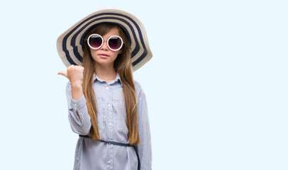 Young blonde toddler wearing hat and sunglasses pointing with hand and finger up with happy face smiling