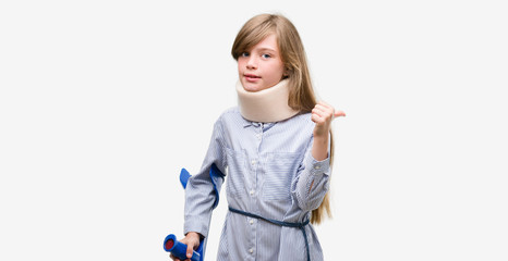 Young blonde child injured wearing neck collar and crutches pointing with hand and finger up with happy face smiling