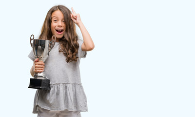 Brunette hispanic girl holding a trophy surprised with an idea or question pointing finger with...
