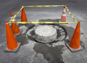 A barricade of caution tape and safety cones mark off maintenance of sewer drainage repair site.