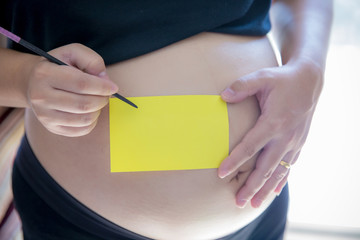 Blank yellow sticker notes on the pregnant woman's belly. FAQ concept. planning and reminder maternity concept. image for copy space, article and illustration.
