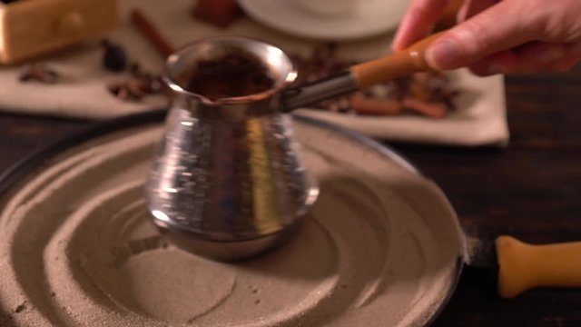 Person swirling a coffee pot on a plate of sand