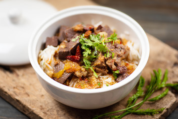 Northern Thai food (Kanom Jeen Nam Ngeaw) in a bowl with vegetables on wooden table, spicy rice noodles soup