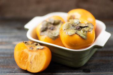 Ripe persimmon in a bowl and sliced persimmon on wooden, healthy fruit