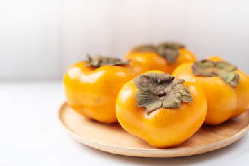 Ripe persimmon on wooden plate and white table, healthy fruit
