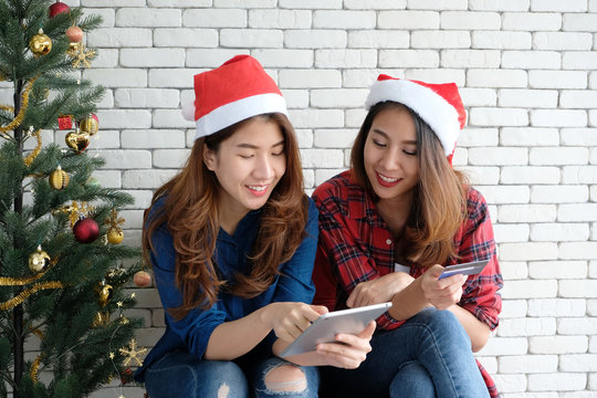 Two young cute asia women holding smartphone and credit card while shopping online with happiness, Christmas holiday shopping concept