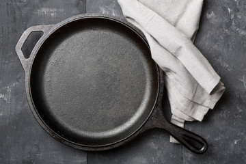 Empty, clean black cast iron pan or dutch oven top view from above on black table with towel