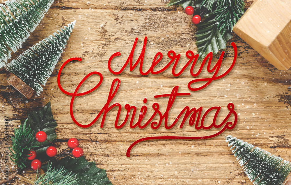 Aufkleber top view of handwriting red merry christmas on rustic wooden table with mini christmas tree and burr
