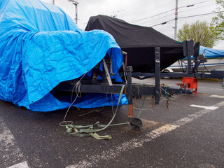 Wide detail of multiple boats on trailers with tarp covers at a parking lot on a wet and stormy day. Nagahama, Shiga, Japan.