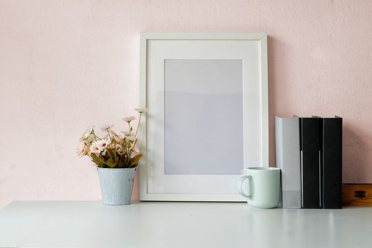 Mockup poster frame, books, dry flower and coffee mug on white desk.
