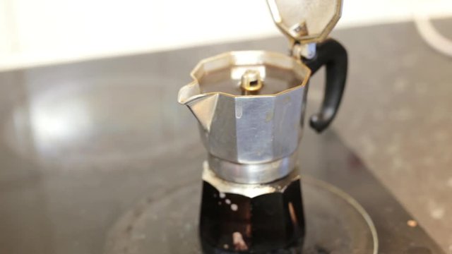 Italian coffee sprinkling out of a moka pot, italian traditional coffee maker, on a induction stove. Good morning symbol.