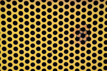 Closeup abstract yellow metal grill with holes pattern 
